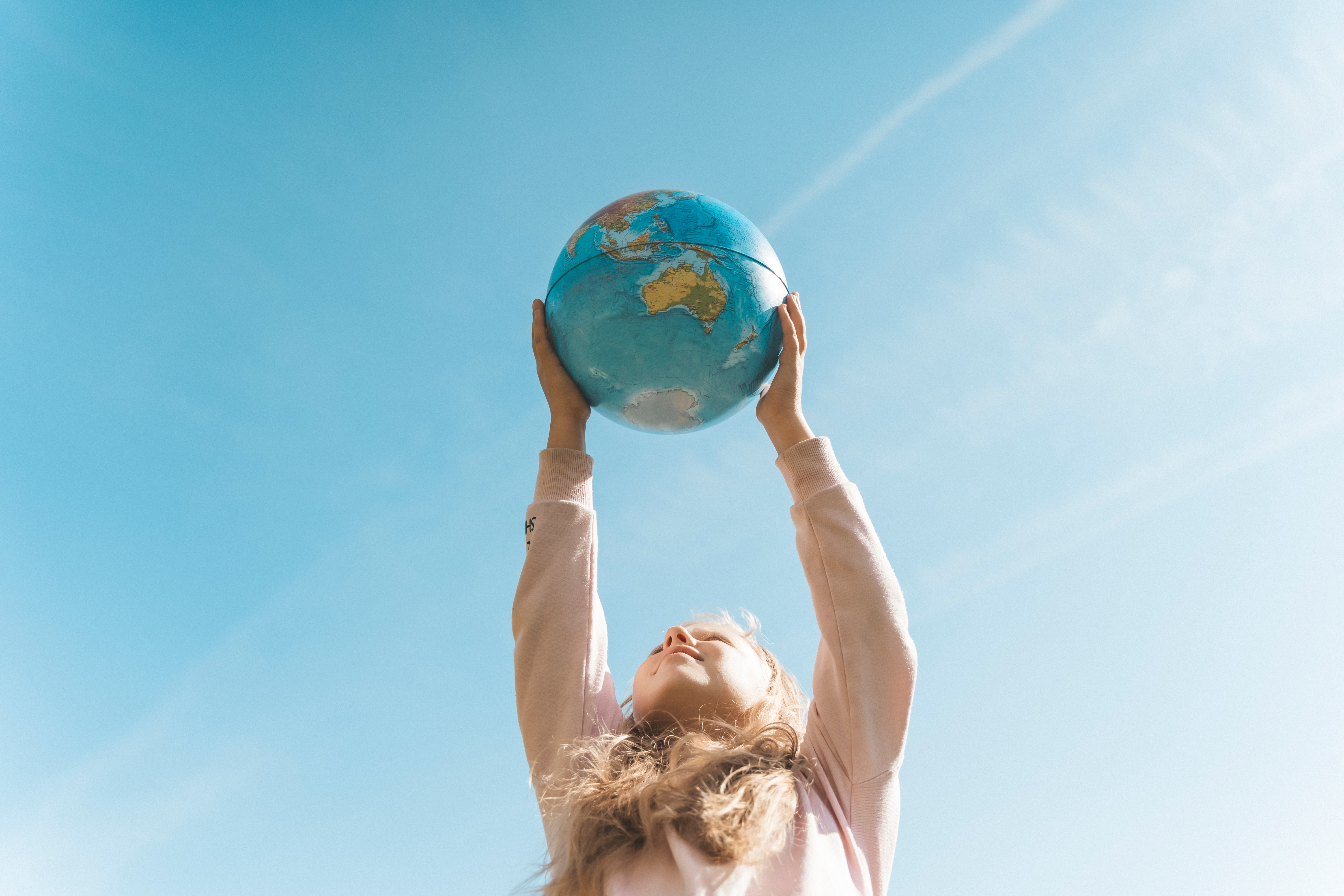 A young girl holds up a globe against a blue sky.